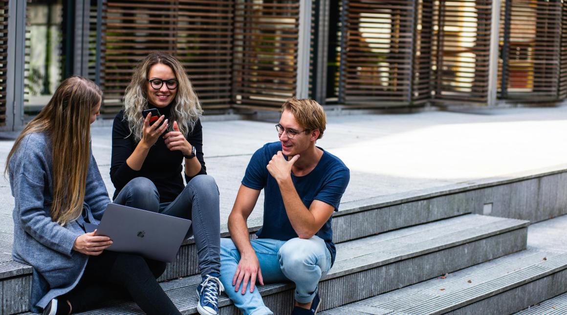 Three students sit on outside steps on a university campus