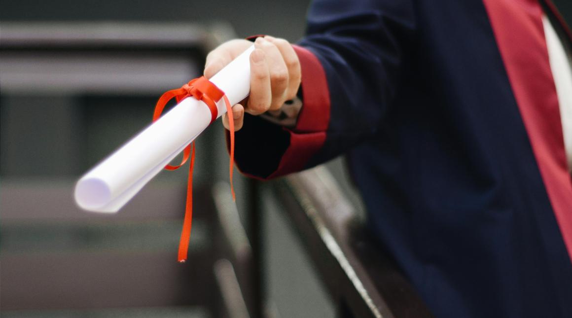 A hand of a graduating student holding a degree scroll