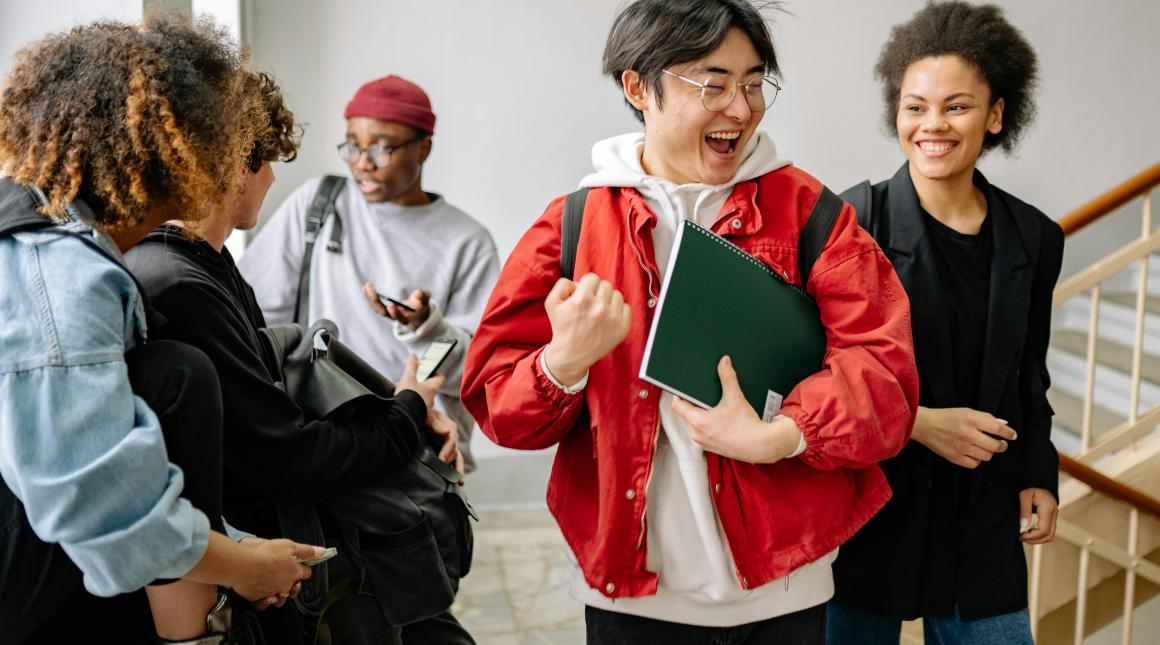 A student makes a fist pump surround by a group of friends, all looking happy and excited