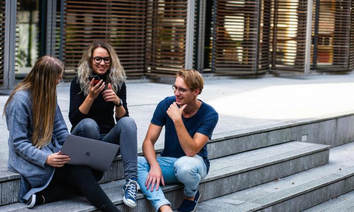 Three students sit on outside steps on a university campus