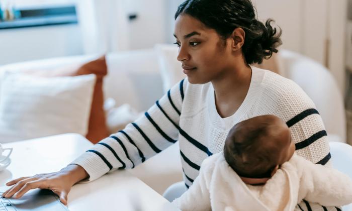 A woman holds her baby while working from home on a laptop