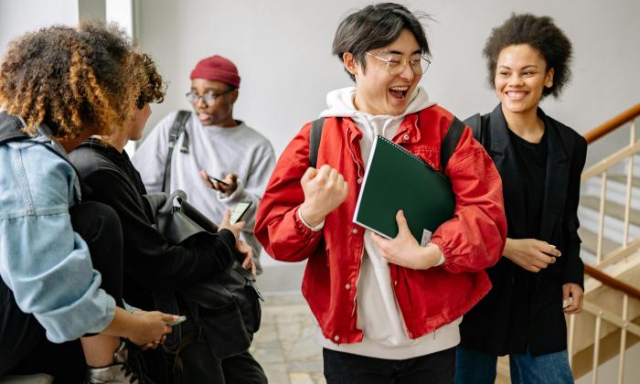 A student makes a fist pump surround by a group of friends, all looking happy and excited