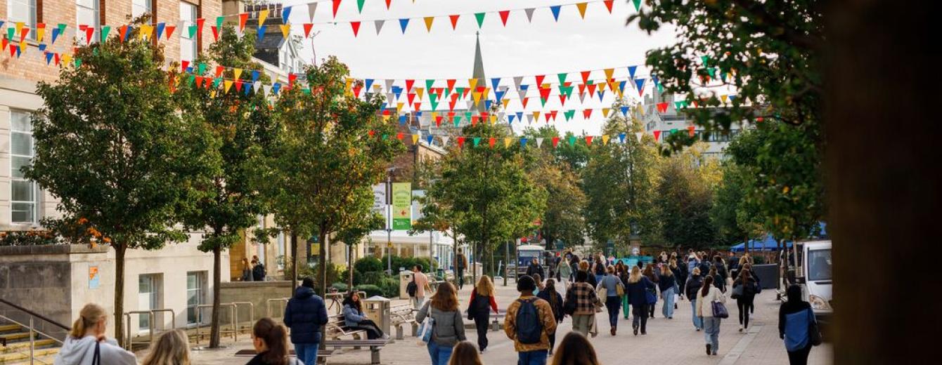 A busy pedestrianised street with groups of students on the University of Leeds campus